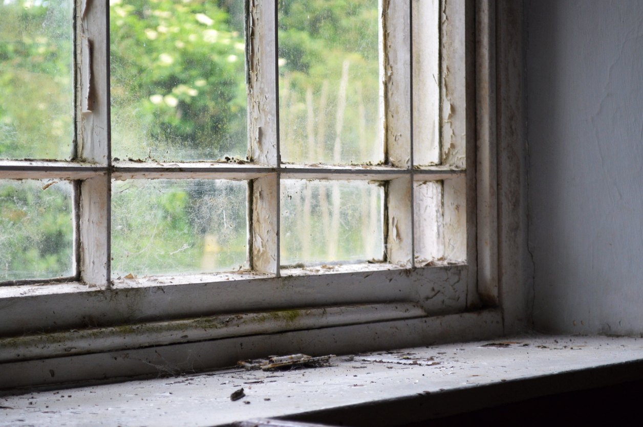 An old window sill with a dirty window and worn surroundingsill