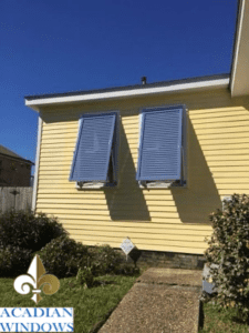 A yellow house with blue Bahama hurricane shutters in New Orleans, installed by Acadian Windows