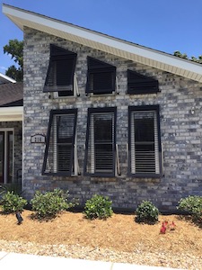 A brick house featuring Acadian's Ocean Springs hurricane shutters in Bahama style, an alternative to roll down hurricane shutters near Ocean Springs.