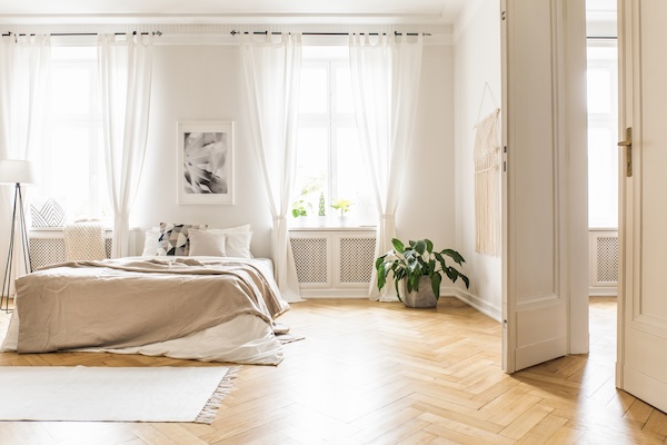 Spacious and bright bedroom interior with beige decorations, hardwood floor, and a book on the window sill seat that begs the question: Is tinting house windows worth it?